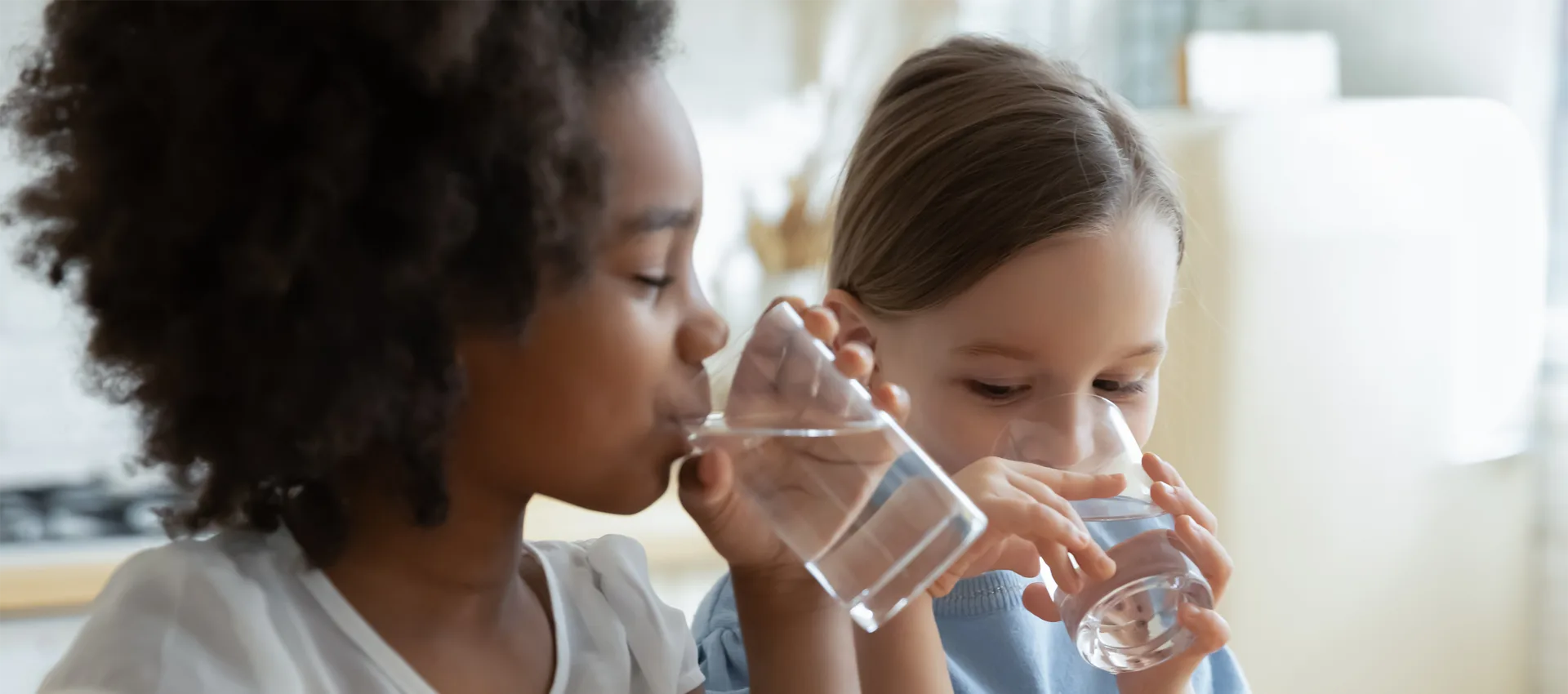 A photo of two children drinking water from glasses. Credit: Adobe Stock