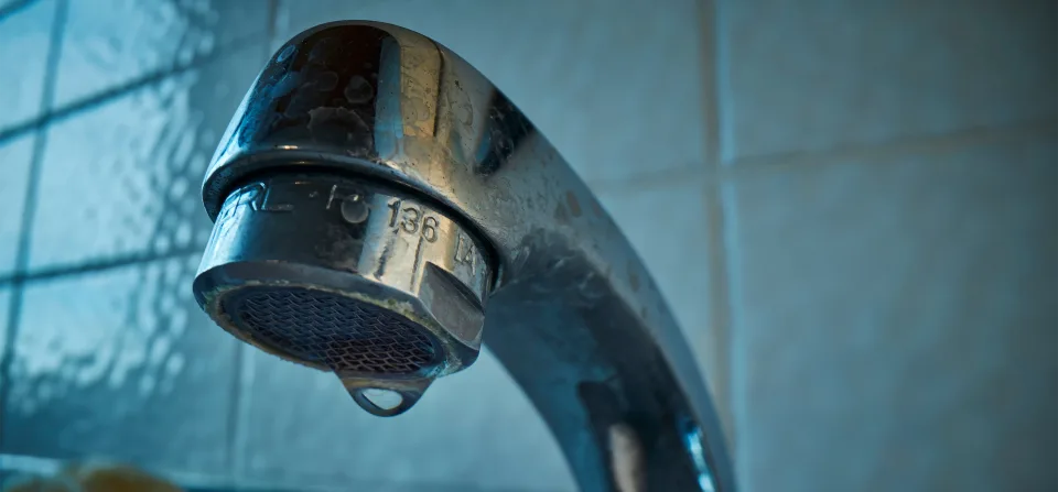 An old, outdated water faucet against blue tile