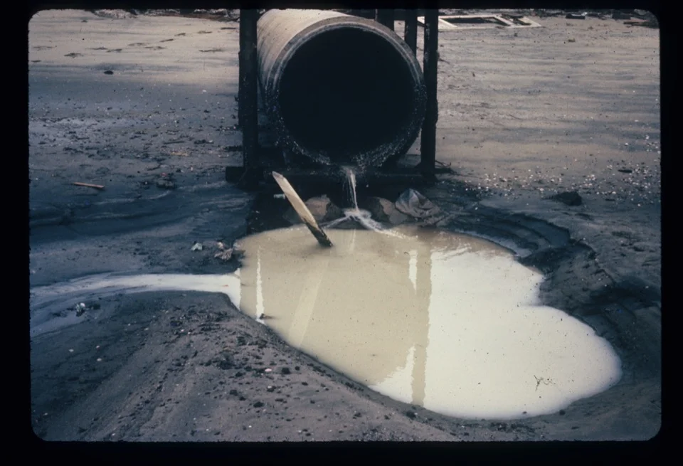 Industrial wastewater discharging from a pipe onto bare ground near San Diego Bay, 1967
