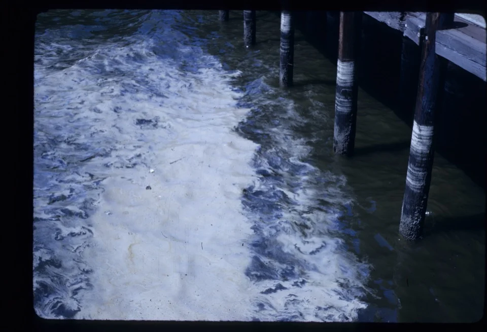 Polluted foam and discharge swirling around pier pilings in San Diego Bay, 1968