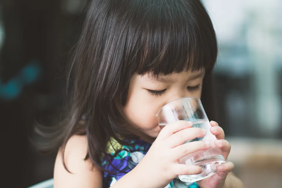 Young child with brunette hair drinking water from a glass